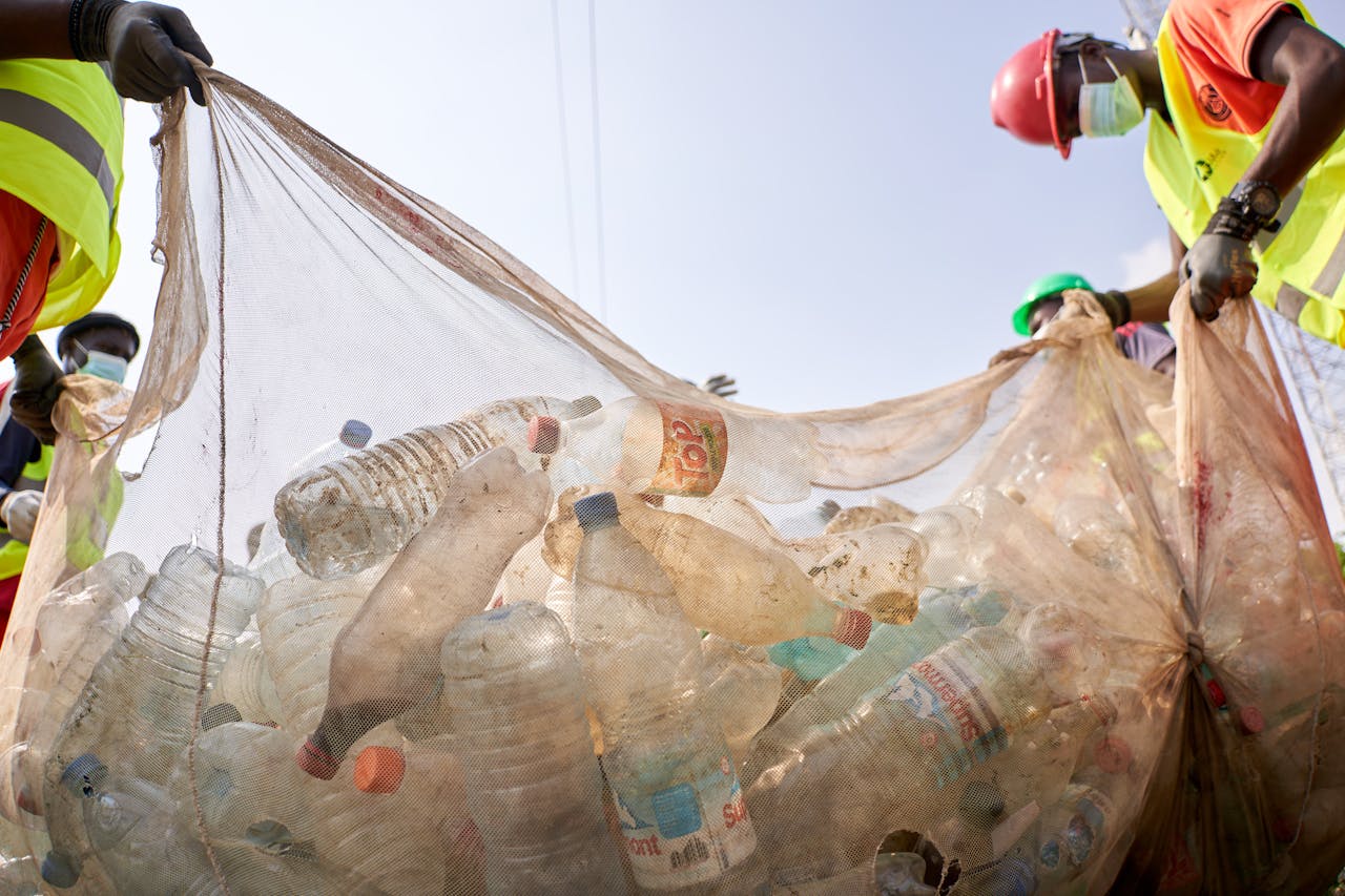 Workers collect plastic bottles and waste outdoors, highlighting environmental action.